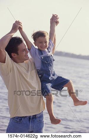 Stock Image - Father lifting his son on the beach. Fotosearch