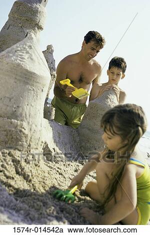 Stock Image - Father making a sand castle on the beach with his son and daughter. Fotosearch