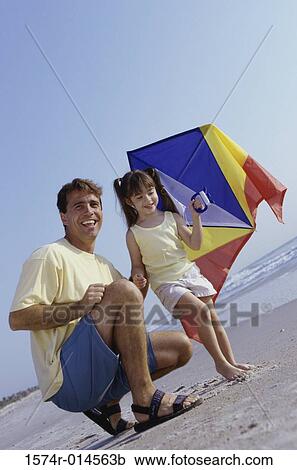 Stock Image - Father with his daughter holding a kite on the beach. Fotosearch