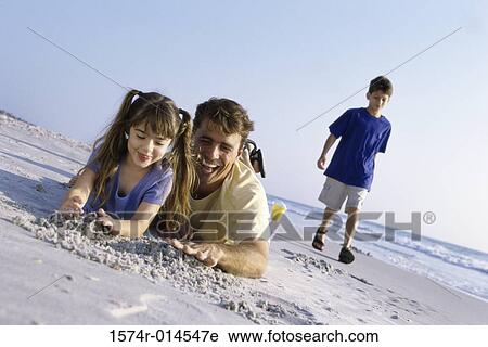 Stock Image - Father with his daughter making a sand castle on the beach. Fotosearch