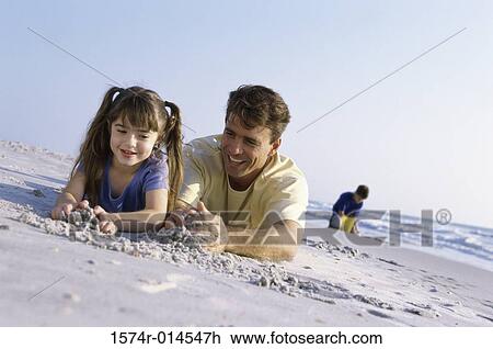 Stock Image - Father with his daughter making a sand castle on the beach. Fotosearch