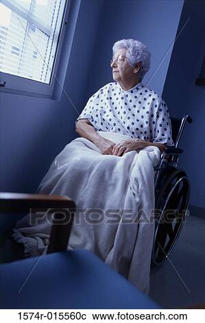 Stock Image - Female patient sitting in a wheelchair looking out of a window. Fotosearch