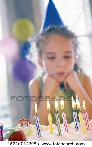 Stock Image - Girl looking at lit candles on a birthday cake. Fotosearch