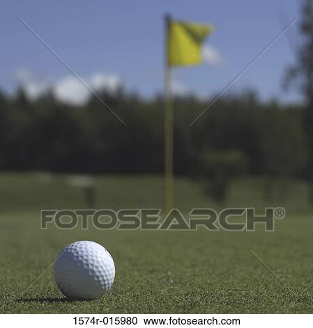 Stock Image - Golf ball on the lawn in front of a flag. Fotosearch