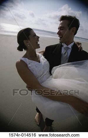 Stock Photograph - Groom carrying his bride on the beach. Fotosearch