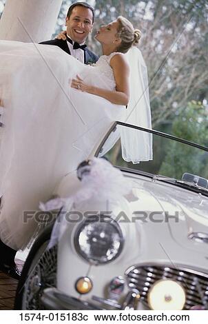 Stock Image - Groom carrying his bride out of a car. Fotosearch
