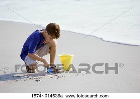 Stock Image - High angle view of a boy digging sand with a shovel on the beach. Fotosearch