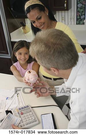 Picture - High angle view of a daughter giving a piggy bank to her father. Fotosearch