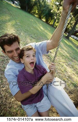 Stock Image - High angle view of a father and son swinging on a rope swing. Fotosearch