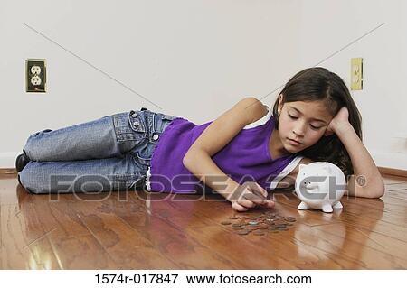 Stock Photo - High angle view of a girl lying on the floor counting coins. Fotosearch