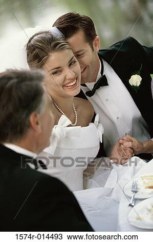 Stock Image - High angle view of a newlywed couple sitting with their father. Fotosearch