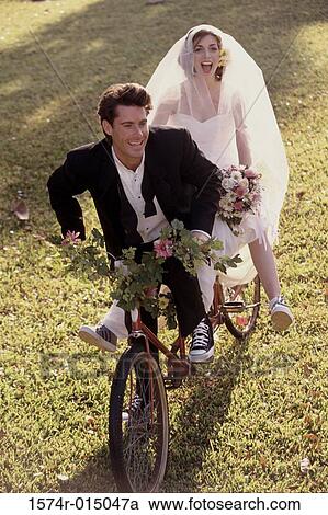Stock Image - High angle view of a newlywed couple riding a bicycle. Fotosearch