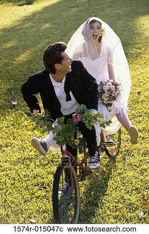 Stock Image - High angle view of a newlywed couple riding a bicycle. Fotosearch