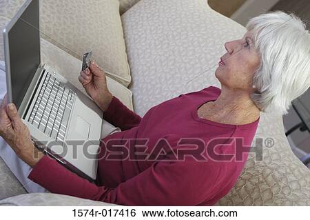 Stock Photograph - High angle view of a senior woman holding a laptop and a credit card. Fotosearch