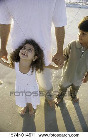 Stock Image - High angle view of a sister and brother holding hands with their father on the beach. Fotosearch