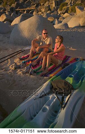 High angle view of a young couple sitting near a boat View Large Photo Image Stock Image - High angle view of a young couple sitting near a boat. Fotosearch