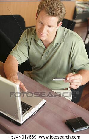 High angle view of a young man using a laptop holding a credit card View Large Photo Image Stock Photo - High angle view of a young man using a laptop holding a credit card. Fotosearch
