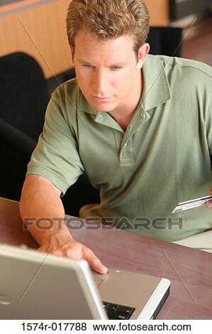 High angle view of a young man using a laptop holding a credit card View Large Photo Image Stock Photo - High angle view of a young man using a laptop holding a credit card. Fotosearch