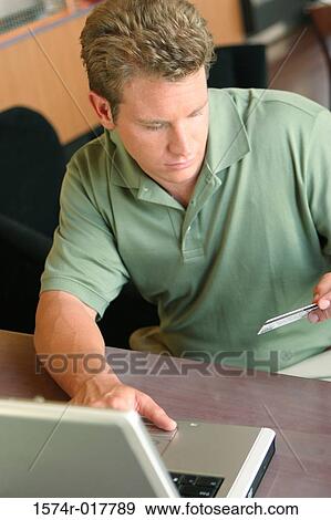 High angle view of a young man using a laptop holding a credit card View Large Photo Image Stock Photo - High angle view of a young man using a laptop holding a credit card. Fotosearch