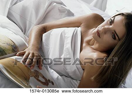 Stock Image - High angle view of a young woman holding a book in bed. Fotosearch