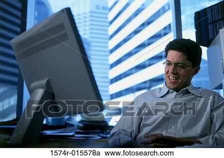 Low angle view of a businessman sitting in front of a computer View Large Photo Image Stock Image - Low angle view of a businessman sitting in front of a computer. Fotosearch