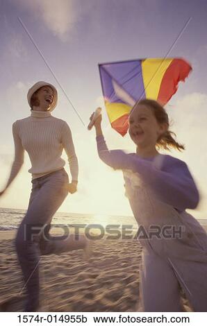Stock Image - Low angle view of a daughter flying a kite with her mother on the beach. Fotosearch