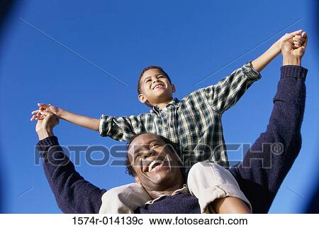 Stock Image - Low angle view of a father carrying his son on his shoulders. Fotosearch