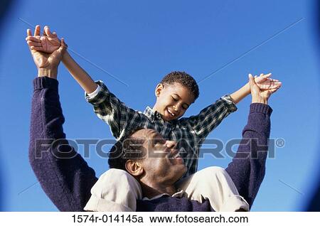 Stock Image - Low angle view of a father carrying his son on his shoulders. Fotosearch