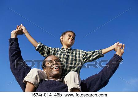Stock Image - Low angle view of a father carrying his son on his shoulders. Fotosearch
