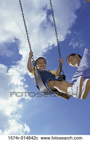 Stock Image - Low angle view of a father pushing his son on a swing. Fotosearch