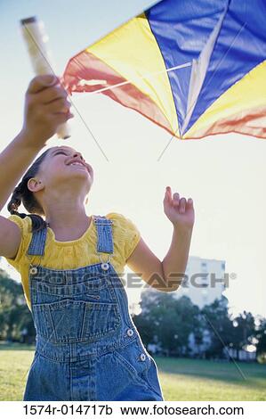 Stock Image - Low angle view of a girl flying a kite. Fotosearch