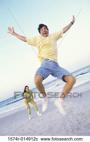 Stock Image - Low angle view of a mid adult man jumping on the beach. Fotosearch