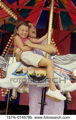 Stock Image - Low angle view of a mother with her daughter sitting on a carousel. Fotosearch