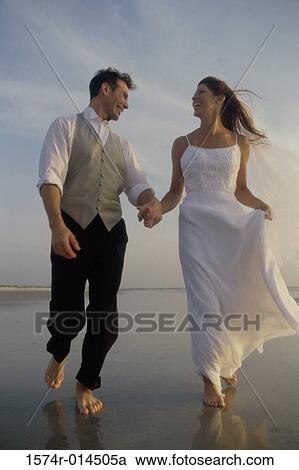 Stock Image - Low angle view of a newlywed couple walking on the beach. Fotosearch
