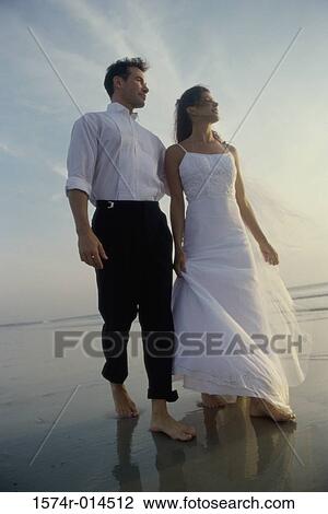 Stock Image - Low angle view of a newlywed couple walking on the beach. Fotosearch