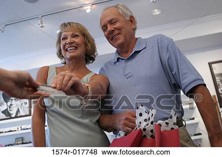 Stock Photo - Low angle view of a senior couple handing a credit card to a person. Fotosearch