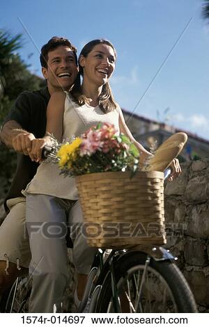 Stock Photo - Low angle view of a young couple riding a bicycle and smiling. Fotosearch