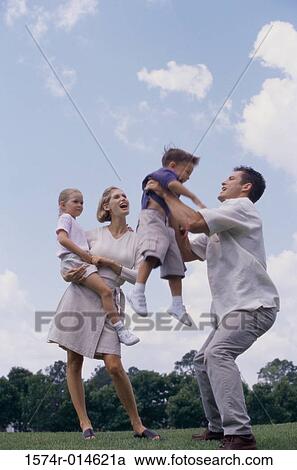 Stock Image - Low angle view of parents playing with their son and daughter in a park. Fotosearch