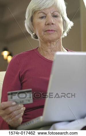 Low angle view of senior woman sitting in front of a laptop holding a credit card View Large Photo Image Stock Image - Low angle view of senior woman sitting in front of a laptop holding a credit card. Fotosearch