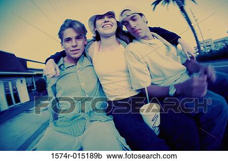 Stock Image - Low angle view of two teenage boys and a teenage girl smiling. Fotosearch