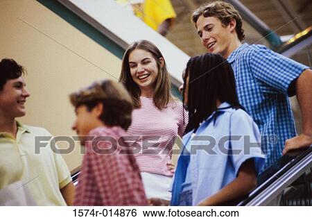 Stock Photograph - Low angle view of two teenage girls and three teenage boys standing on an escalator. Fotosearch