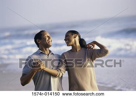 Stock Image - Mid adult couple holding hands on the beach. Fotosearch