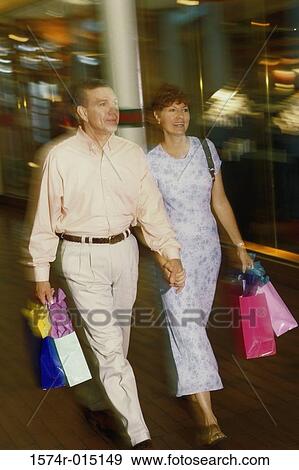 Stock Photo - Mid adult couple holding shopping bags walking on a road. Fotosearch