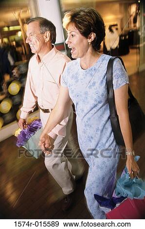 Mid adult couple holding shopping bags walking on a road View Large Photo Image Stock Photo - Mid adult couple holding shopping bags walking on a road. Fotosearch