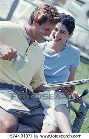 Mid adult man reading a newspaper with a woman sitting beside him View Large Photo Image Stock Image - Mid adult man reading a newspaper with a woman sitting beside him. Fotosearch