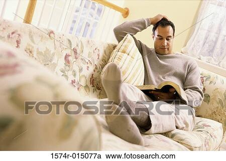 Mid adult man sitting on a couch reading a book View Large Photo Image Stock Image - Mid adult man sitting on a couch reading a book. Fotosearch
