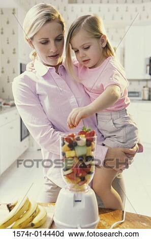 Stock Image - Mother carrying her daughter in front of a blender. Fotosearch