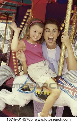 Stock Image - Mother with her daughter sitting on a carousel. Fotosearch