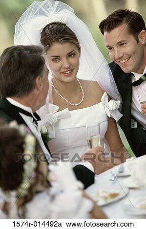 Stock Image - Newlywed couple sitting with their parent and a flower girl. Fotosearch