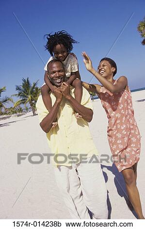 Stock Image - Parents and their daughter walking on the beach. Fotosearch